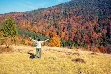 Elleri havada bir adam sonbaharda dağın kenarında duruyor.