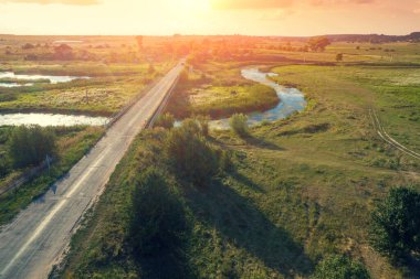 Kırsal alan. Hava görüntüsü. Gün batımında dolambaçlı nehrin üzerindeki köprü. Yukarıdan görüntüle