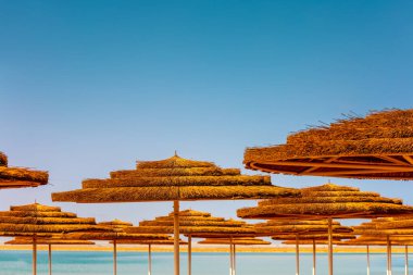 Güneş şemsiyeli tropik plaj manzarası. Güneşli bir günde kumsalda saman güneş şemsiyeleri. Yaz mevsimi, tatil kavramı