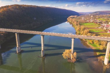 Güneşli bir sonbahar gününde Dinyester nehri, tepeler ve Ustechko köyünün üzerindeki yol köprüsünün hava manzarası.