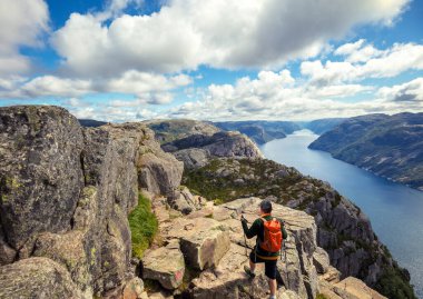Uçurumun tepesine tırmanan bir adam. Bulutlu bir günde güzel Lysefjord manzarası. Muhteşem Lysefjord 'un Rocky Shore' u. Norveç 'in güzel vahşi doğası