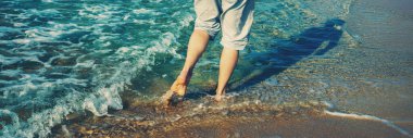A young man barefoot walks on the beach. Horizontal banner