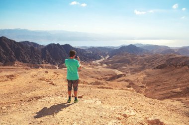 Bir adam dağ çölünde seyahat eder. Adam cep telefonuyla güzel bir çöl manzarasının fotoğrafını çekiyor. İsrail, Negev Çölü 'nde Eilat Dağları rezervi