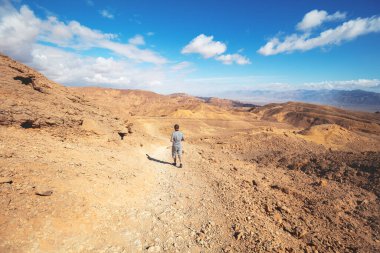 Genç adam güneşli bir günde çölde yürüyüş yapıyor. İsrail 'in Negev çölündeki Eilat dağları