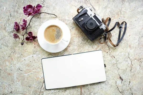 Cup of coffee, orchid, old retro analog camera, notepad flat lay on marble table