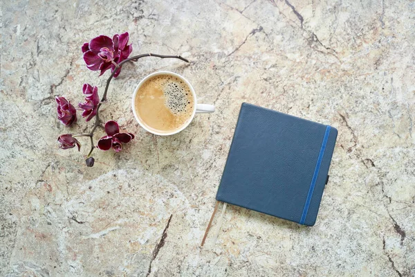 Cup of coffee, orchid, notepad flat lay on marble table