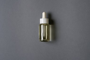 Gri zemin üzerinde yağ bulunan şeffaf düz bir kozmetik şişesi