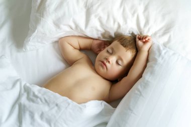 Yeni yürümeye başlayan beyaz beyaz beyaz çocuk beyaz yatakta uyuyor..