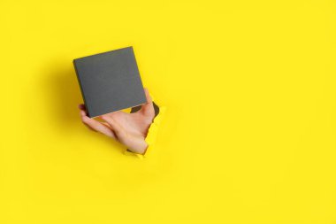 Sarı kağıttaki delikten küçük koyu gri kutuyu tutan kadın. 