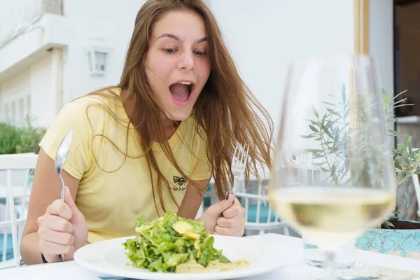 Молодая красивая девушка ест салат со смешным лицом в желтой футболке — стоковое фото