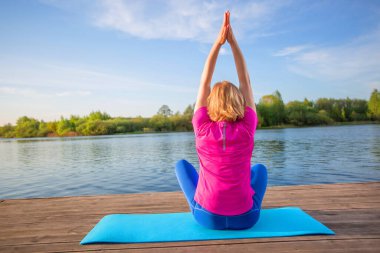 Yoga yapan bir kadın nehir kıyısındaki bir halıya asanas sergiliyor..