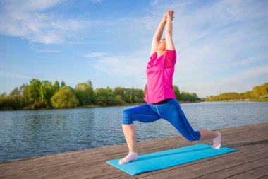 Yoga yapan bir kadın nehir kıyısındaki bir halıya asanas sergiliyor..