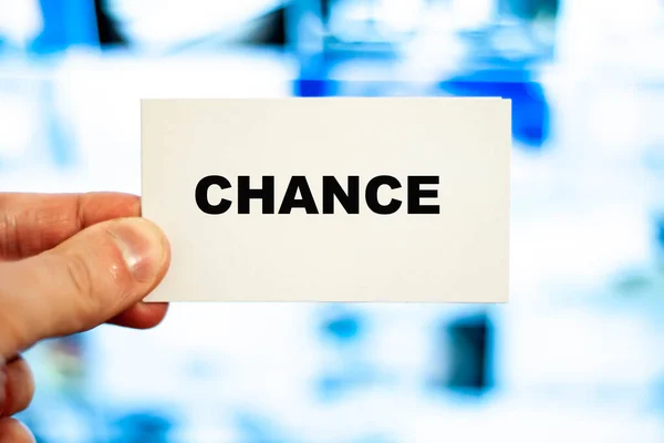 The word chance in large letters on the business card. White paper in hand on a blue background.