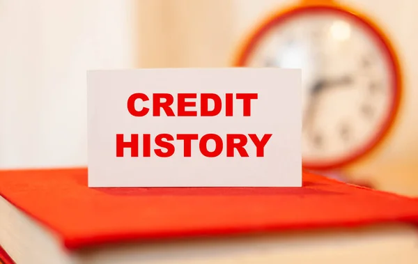 CREDIT TARİHİ kırmızı defter üzerine beyaz kağıt üzerine yazı. Alınan kredilerin geçmişi zaman arkaplanına göre.