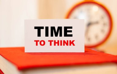 Kapalı bir kitap üzerinde düşünme zamanı. Arka planda yuvarlak bir saat var..