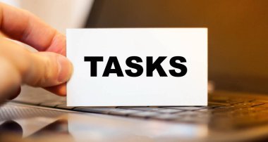 İş adamı, iş gününden önce bilgisayarın arka planında TASKS ile kağıt tutuyor..