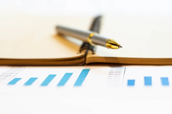 A silver business pen with a golden tip with a blurred background lies on a notebook