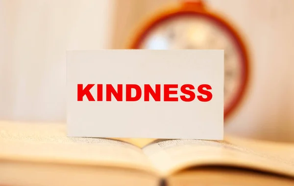 The word KINDNESS on an open blurred book with a clock in the background