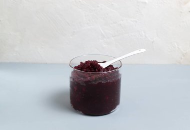 Cam kavanozda pancar reçeli ve gri bir arka planda çay kaşığı. Boşluğu kopyala.