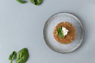 Gri arka planda gri bir tabakta taze yapraklı ıspanak ve muzlu krep. Sağlıklı gıda konsepti. Yatay oryantasyon. Uzayı kopyala Üst görünüm.