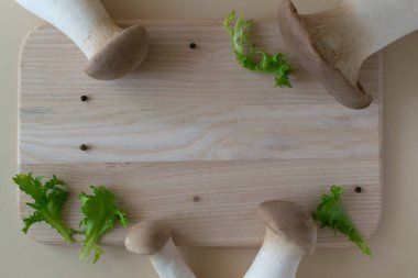 Pastel arka planda ahşap kesim tahtasının üzerinde marul yaprakları olan Eringi mantarları. Pleurotus eringi. Sağlıklı gıda konsepti. Yatay oryantasyon. Düz yat. Boşluğu kopyala.