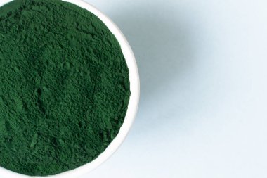 Mavi arka planda beyaz bir kasede klorella tozu ve metin için yer var. Sağlıklı gıda konsepti. Yatay yönelim.