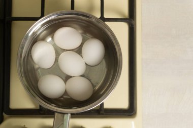Beyaz tavuk yumurtaları, ev mutfağındaki ocakta suyla birlikte bir kepçede kaynatılır. Sağlıklı gıda konsepti. Horisontal oryantasyon. Üst görünüm.