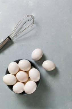 Beyaz tavuk yumurtaları gri bir kasede yatar ve gri arka planda çırpar. Diyet gıda konsepti. Uzayı kopyala Üst görünüm.