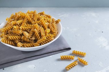 Gri arka planda gri bir peçete üzerinde beyaz bir kasede çiğ fusilli. İtalyan mutfağı konsepti. Uzayı kopyala Yatay oryantasyon. Tam tahıllı makarna.