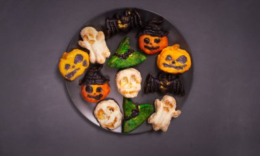 Cadılar Bayramı için süzme peynirli keklerin adım adım hazırlanması. Siyah tabakta çocuklar için canavarlı tatlı kekler. Renkli balkabakları, kafatasları, hayaletler, yarasalar ve cadı şapkaları. Üst görünüm.