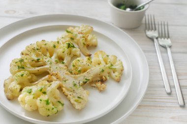 Beyaz ahşap arka planda beyaz bir tabakta chimichurri soslu karnabahar. Vejetaryen ve vejetaryen yemeği kavramı. Sağlıklı beslenme. Yatay oryantasyon. Seçici odak.