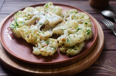 Ahşap bir arka planda seramik tabakta chimichurri soslu karnabahar. Vejetaryen ve vejetaryen yemeği kavramı. Sağlıklı beslenme. Dikey oryantasyon. Seçici odak.