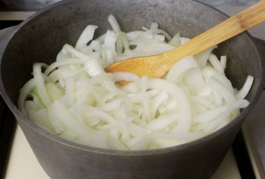 Fransız soğan çorbası pişirme süreci. Soğanlar ocaktaki tencerede yarım halkalar halinde kesilmiş. Geleneksel mutfak konsepti. Yatay oryantasyon. Seçici odak.