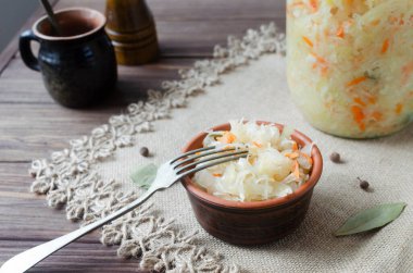 Geleneksel lahana turşusu, içinde havuç ve baharat olan bir kâse ve ahşap bir masada cam bir kavanoz. Otantik Avrupa mutfağı, sağlıklı yeme ve mayalanmış gıdaların bir sembolü. Seçici odak
