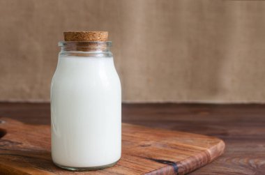 Taze kefir ile dolu, mantar tıpası ile mühürlenmiş, çuval bezine yerleştirilmiş bir cam şişenin kırsal bir fotoğrafı. Mayalanmış süt ürünleri konsepti. Yatay oryantasyon. Seçici odaklanma. Boşluğu kopyala