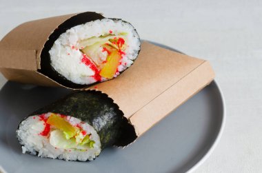 İçinde pirinç, deniz ürünleri, marul, krem peynir ve tobiko bulunan deniz yosunu ve kağıt kollara sarılı iki suşi burrito. Füzyon gıda konsepti suşi geleneği ve burrito stilini birleştiriyor..
