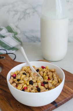 Sağlıklı kahvaltı kasesi gevrek gevrek, tahıl gevreği, mısır gevreği ve ahşap tahta üzerinde kurumuş böğürtlen. Yoğurt, kaşık ve çizgili kumaşlı yaşam tarzı yemek fotoğrafçılığı konsepti.