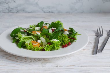 İki çatal ve peçeteyle bembeyaz bir tabakta yeşil, mandalina, feta peyniri, nar ve badem salatası, açık arkaplan. Sağlıklı beslenme konsepti. Temiz yemek..
