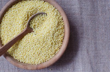 Çiğ Groats - Çuval bezi arka planında tahta bir kasede darı. Kırsal tarzda. Vejetaryen, vejetaryen, sağlıklı ve sağlıklı yemekler. Cesaret dostu bir kavram. Geçmişi. Yatay oryantasyon. Üst Manzara. Boşluğu kopyala