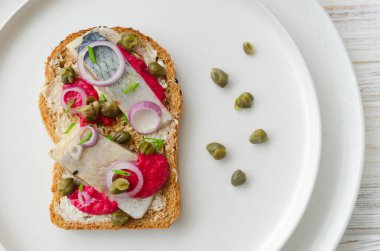 Geleneksel İskandinav usulü salamura ringa balığı, parlak pancar kreması, ince kırmızı soğan halkaları, kapari. Açık sandviç ve uyumlu renk kombinasyonu. Üst görünüm