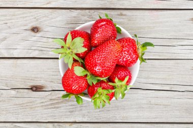 Gri ahşap masa üzerinde basit bir beyaz kase taze olgun çilek