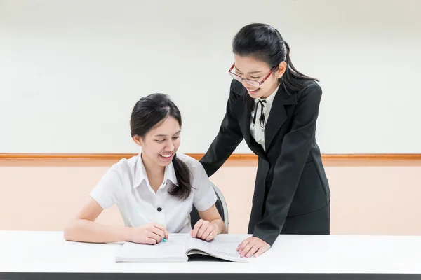 Učitelé něco na asijská studentka v uniformě v classroo — Stock fotografie