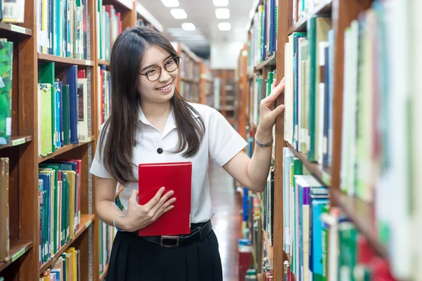 Asiática estudiante en uniforme de lectura en la biblioteca en la universidad — Foto de Stock