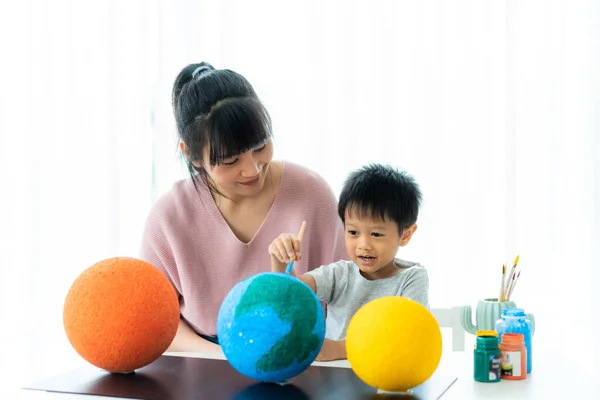 Asian preschool student boy with mother painting the moon learning about the solar system at home, Homeschooling and distance learning