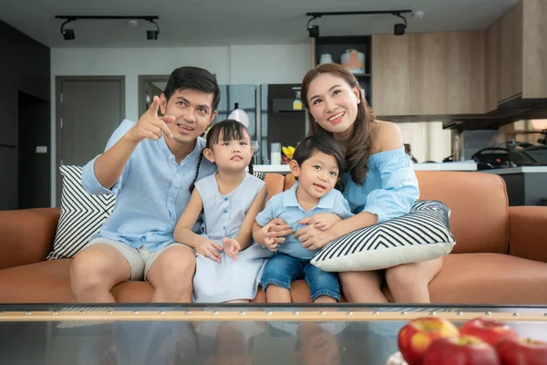 Asian happy family sitting and watching television in living room at home and spent quality time together for activity in vacation day, holiday, happiness or lifestyle concept