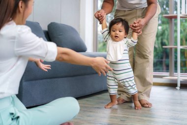 Asyalı bebek ilk adımı atarak annesine doğru yürüyor. Mutlu küçük bebek babasıyla yürümeyi öğreniyor yardım ediyor ve nazikçe eve yürümeyi öğretiyor.