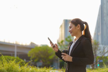 Asyalı yönetici kadın elinde kahve fincanı ve sokakta cep telefonu kullanıyor. Bangkok, Tayland 'da ofis binaları var.