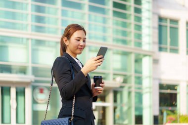 Asyalı yönetici kadın elinde kahve fincanı ve sokakta cep telefonu kullanıyor. Bangkok, Tayland 'da ofis binaları var.