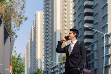 Asyalı işadamı, sabah işe gidip gelirken iş arkadaşıyla telefonda konuşuyor.
