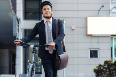 Asyalı işadamı sabah bisikletini evden itip işe bisikletle gitmeye hazırlanıyor. Eko aktarımı